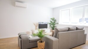 A modern living room with a grey sectional sofa, a small side table, a flat-screen TV, and two potted plants. - 3 bedroom apartment near the center of Ponte de Lima with private parking (Ponte de Lima)