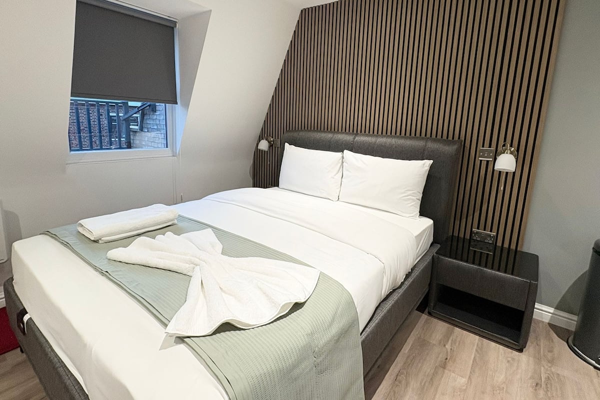 Et moderne hotelværelse med en stor seng, et vindue med udsigt, et natbord med lampe og en væg af træpaneler.