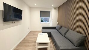 Una sala de estar moderna con un sofá gris, una mesa de centro blanca y un televisor de pantalla plana montado en la pared.