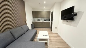 Una sala de estar moderna con un sofá gris, una mesa de centro blanca y un televisor montado en la pared.