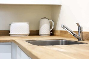 A kitchen with a wooden countertop, a stainless steel sink, and two white appliances.