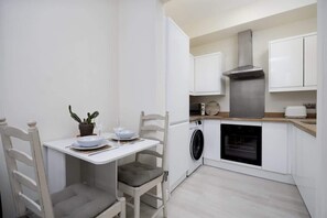 A compact kitchen with a washing machine, oven, and a dining area with chairs and a table.