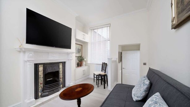 Una sala de estar con chimenea, televisor montado encima, sofá y mesa de comedor.