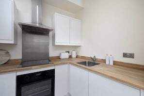 A modern kitchen with stainless steel appliances, white cabinetry, and a wooden countertop.
