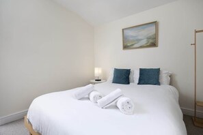 A hotel room with a neatly made bed, a bedside lamp, and a painting on the wall.