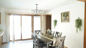 A dining area with a wooden table and chairs, a chandelier, and a 'gather' sign on the wall.
