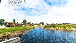 A riverside view with a wooden dock, a grassy area, and buildings in the background.