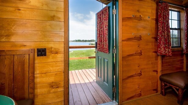 A wooden cabin with a green door, a wooden deck, and a view of a lake.