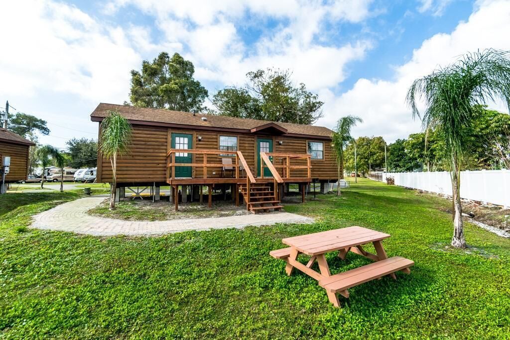 Une cabane en bois dotée d’une terrasse et d’une table de pique-nique, située dans un espace verdoyant.