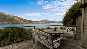 A wooden deck with a round table and chairs, overlooking a lake with mountains in the background. - Perfect on Perkins - Lake views (Queenstown)