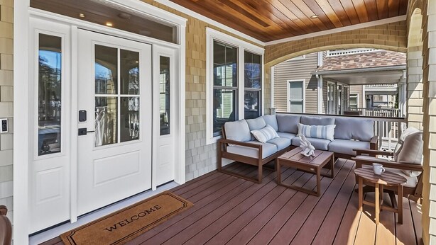 Eine überdachte Veranda mit Holzboden, einem grauen Sofa und einer weißen Tür mit Fußmatte.