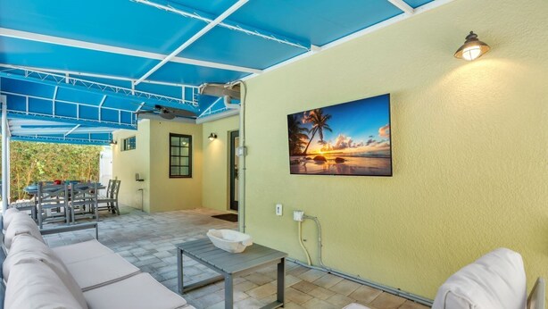 Une terrasse extérieure dotée d’un espace salon abrité, d’une table et d’un tableau accroché au mur.