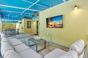 Een terras buiten met een overdekte zithoek, een tafel en een aan de muur hangend schilderij.