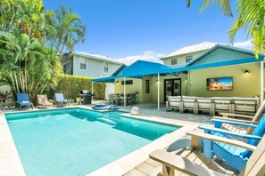 Ein Garten mit Schwimmbad, Liegestühlen, Grill und überdachter Terrasse.