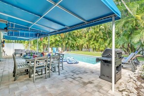 Eine Terrasse im Freien mit überdachter Sitzecke, einem Pool und einem Grill.