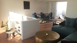 Ett vardagsrum med en soffa, ett runt bord med en växt, en matplats med stolar och en trappa.