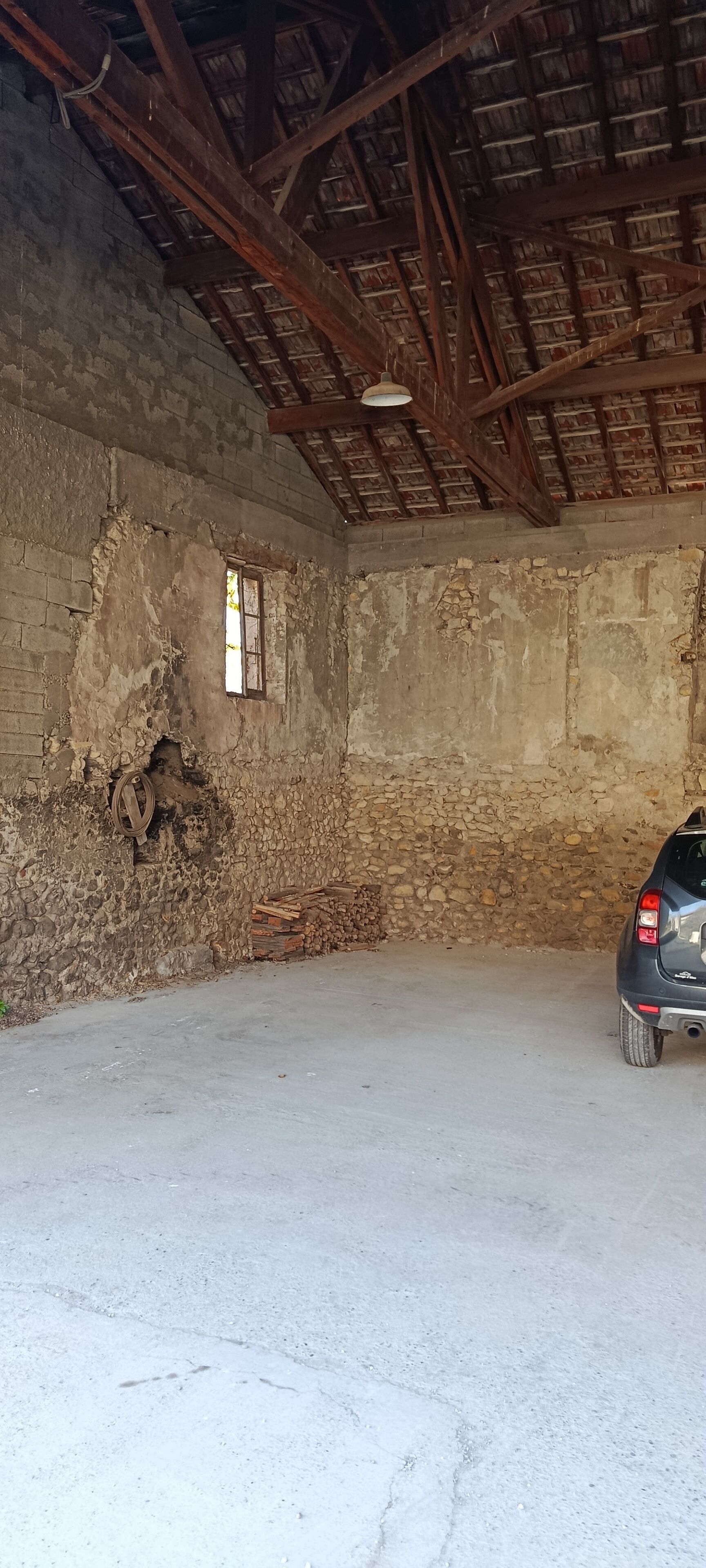 A room with a concrete floor, a car parked inside, and a rustic wooden ceiling with exposed beams.