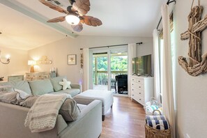 Ein gemütliches Wohnzimmer mit einer Couch, einem Fernseher, einem Deckenventilator und Blick ins Freie.
