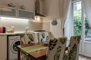 A compact kitchen with a washing machine, a dining table with chairs, and a view of greenery outside. - Florence Apartment with Patio in the City Center (Firenze)