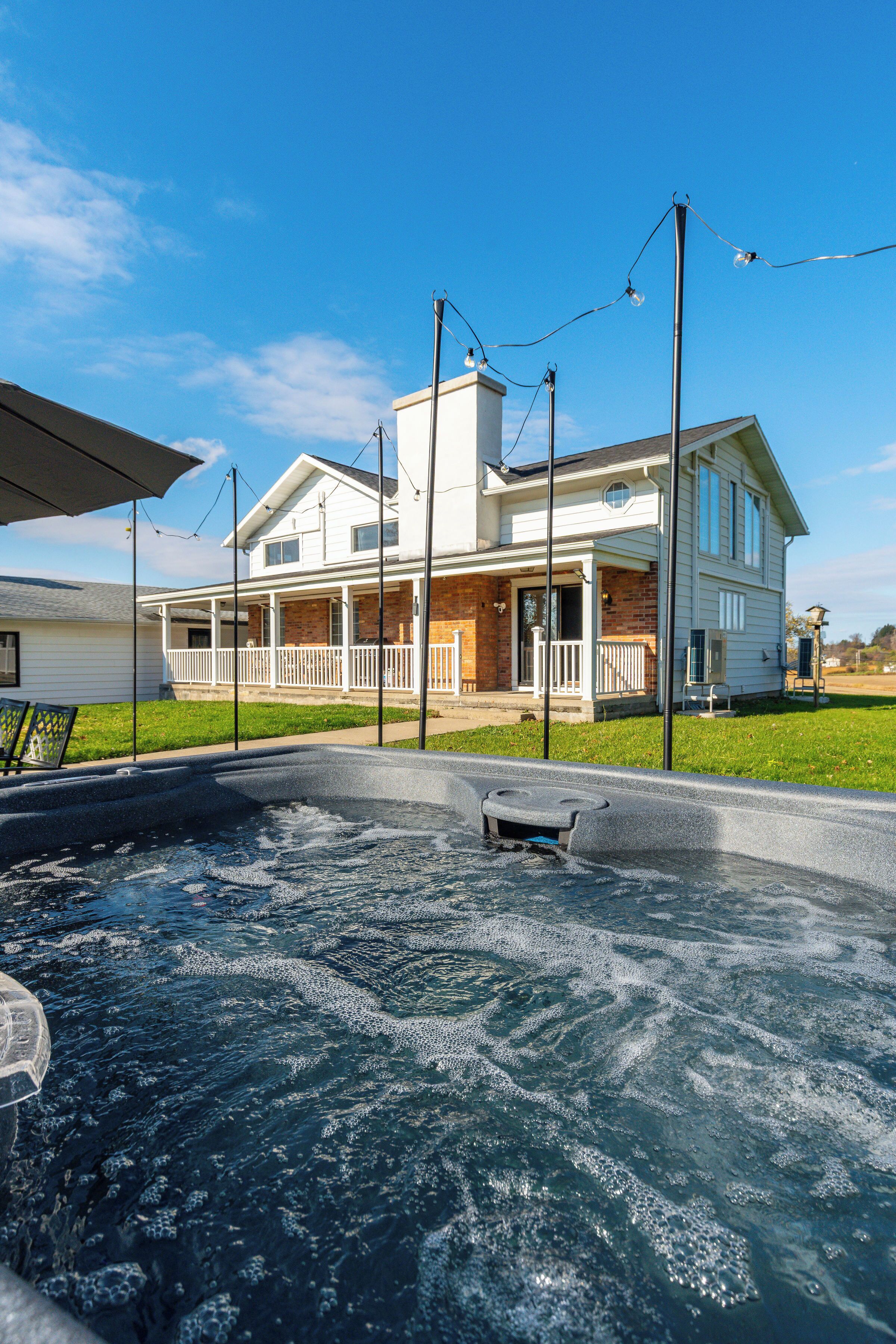 A house with a large outdoor hot tub, a covered patio, and a well-maintained lawn.