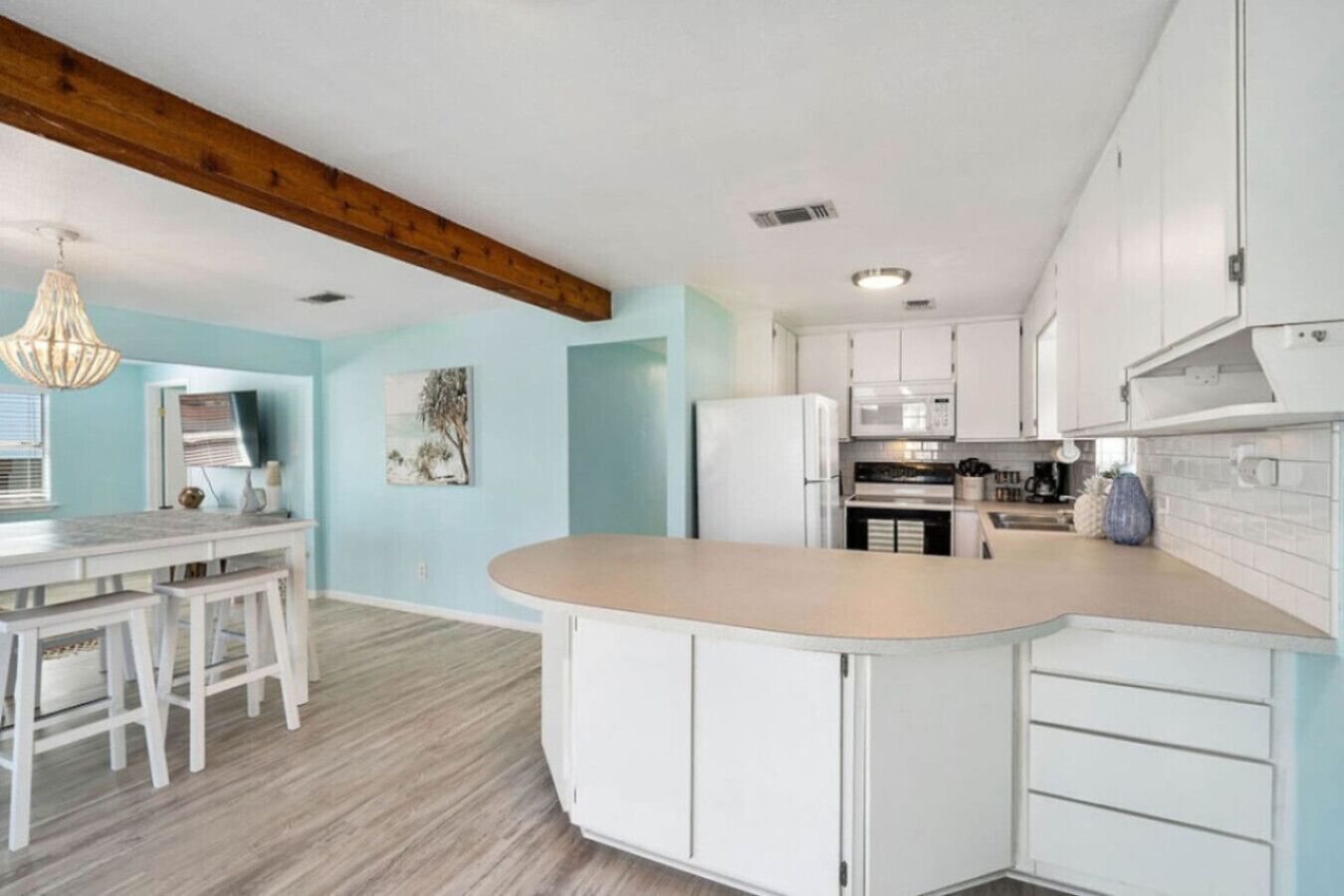 Una cucina moderna con mobili bianchi, un'isola centrale e una trave in legno al soffitto.