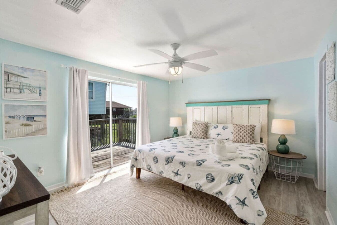 Une chambre à coucher avec un lit, deux tables de chevet avec des lampes, un ventilateur de plafond et une vue sur un balcon.