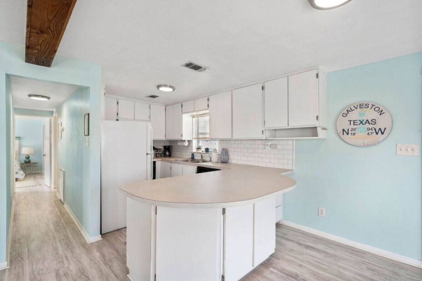 Cocina con armarios blancos, una isla central y un reloj de pared que muestra coordenadas de Galveston, Texas.