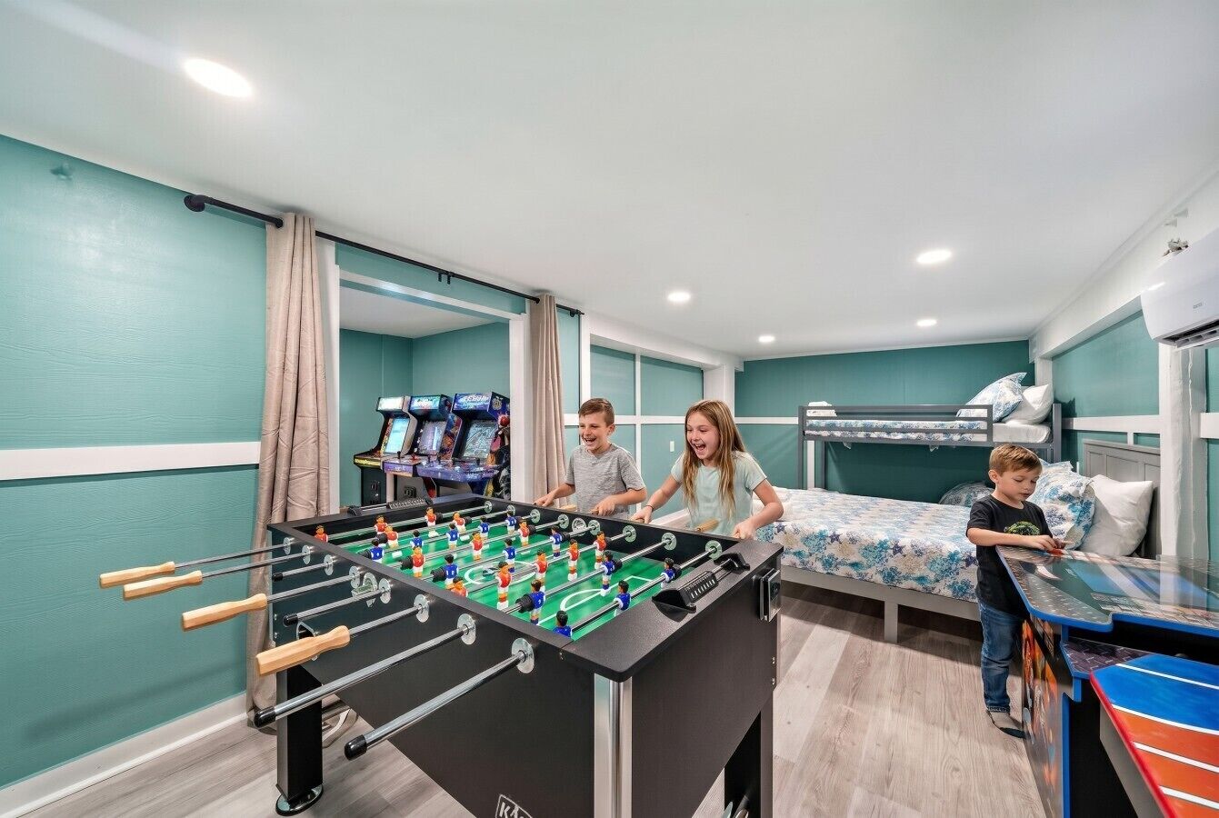 A room with a foosball table, a bed with a floral bedspread, and a television screen.