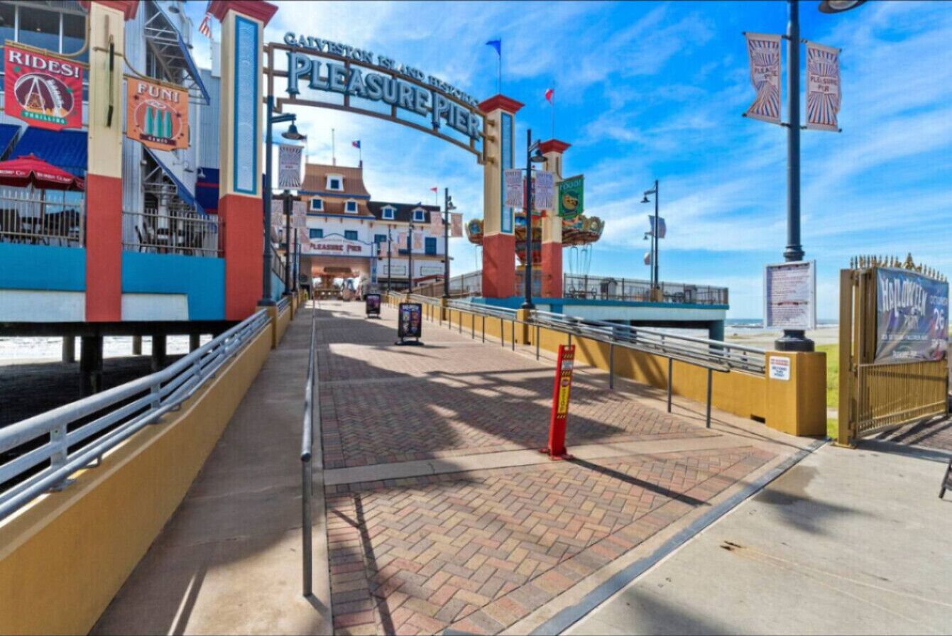 Une promenade en bois avec une pancarte indiquant « Pleasure Pier » et divers magasins et attractions.