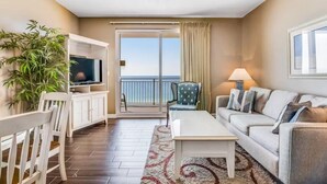 A living room with a TV, a sofa, a coffee table, a chair, a lamp, a plant, and a balcony with a view of the sea. - Sterling Reef 405 (Panama City Beach)