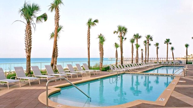 A pool area with lounge chairs and palm trees, overlooking the sea. - Sterling Reef 405 (Panama City Beach)