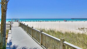 A wooden boardwalk leading to a beach with clear blue water and a pier in the distance. - Sterling Reef 405 (Panama City Beach)