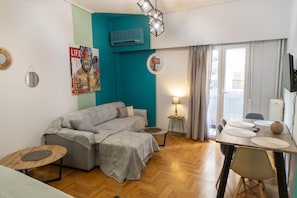 Una sala de estar con sofá, una mesa de comedor con sillas, televisor y ventana con cortinas.