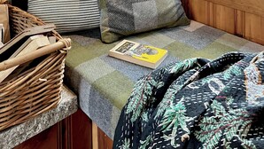 A cozy cabin-style room with a wooden interior, a window with a view of greenery, a bed with patterned bedding, a bedside lamp, and a wicker basket. - Stay at adorable mill house in walkable Maynard. Small but well-designed spaces. (Maynard)