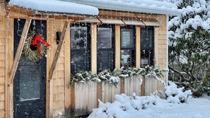 A wooden house with a snow-covered roof and a front door with a wreath. - Stay at adorable mill house in walkable Maynard. Small but well-designed spaces. (Maynard)