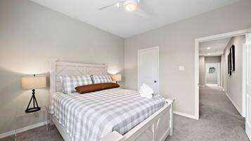 Un dormitorio con cama, lámparas de noche, ventilador de techo y una puerta que da a otra habitación.
