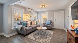 A living room with a gray sofa, a round coffee table, and a TV on a wooden cabinet. - Charming Home in Perfect Central Spot (Galveston)