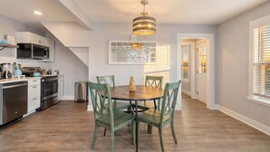 A modern kitchen with a dining area, featuring a round table and four chairs, a built-in oven, and a hanging light fixture. - Charming Home in Perfect Central Spot (Galveston)