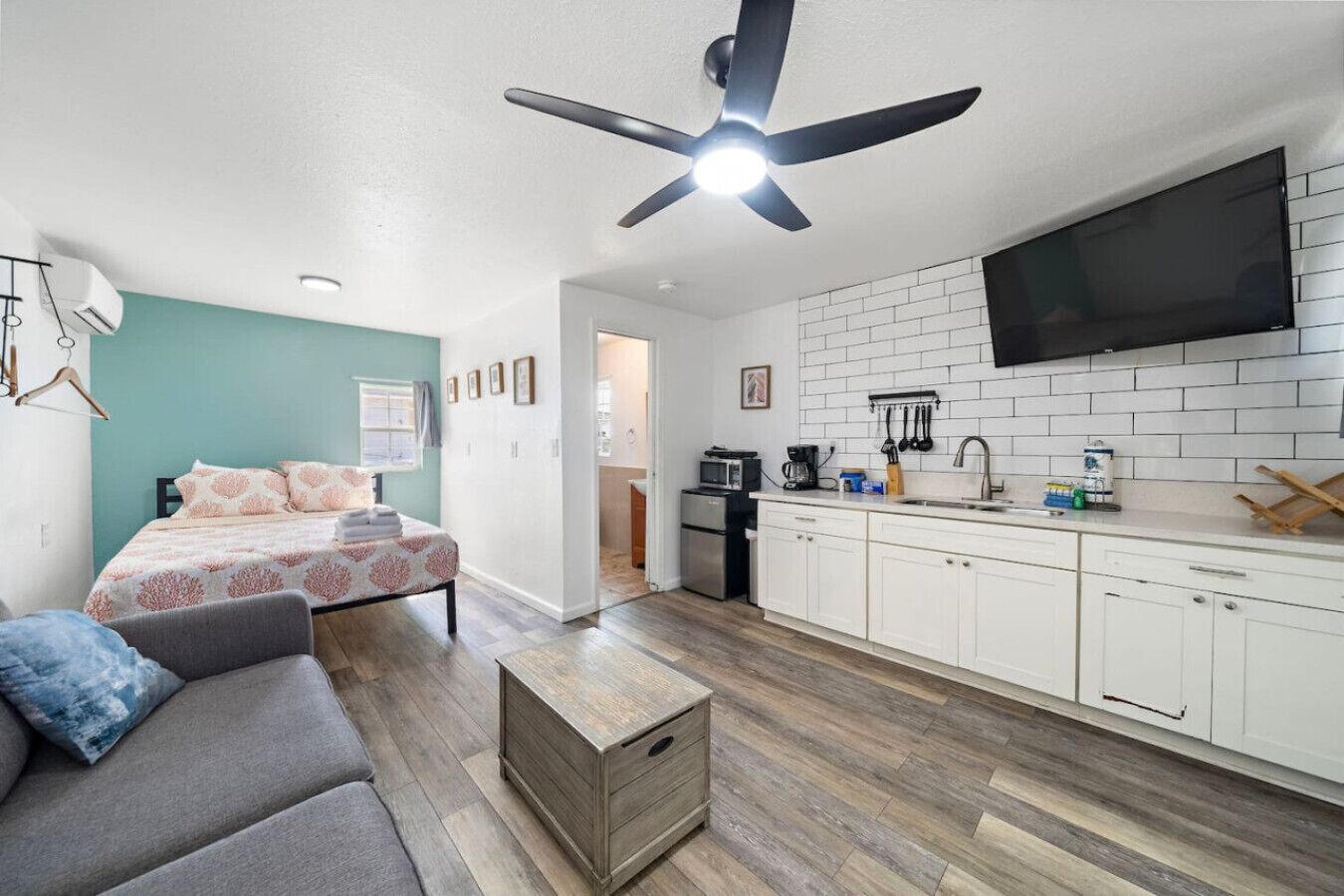 Une chambre moderne avec un lit, un canapé gris, une commode en bois et un ventilateur de plafond.