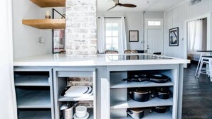 A modern kitchen with white cabinetry, a brick accent wall, and a central island with a sink. - Historic Galveston Homes Near Everything (Galveston)