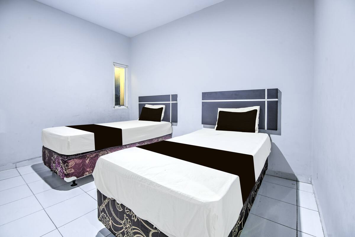 A hotel room with two single beds, a window, and a tiled floor.