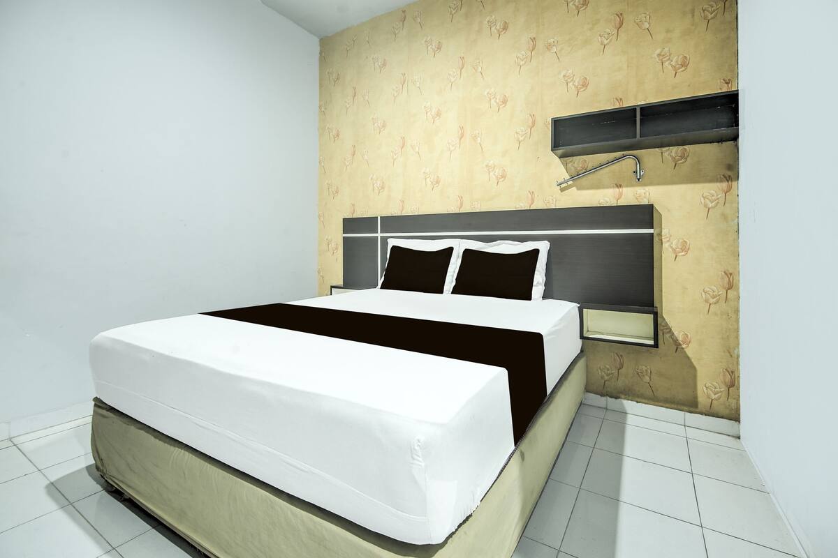 A neatly made bed with a headboard, a bedside table, and a wall-mounted shelf.