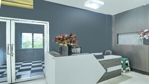 Zona de recepció amb un terra de pissos, un taulell de recepció, un tamboret verd i una finestra amb vistes.