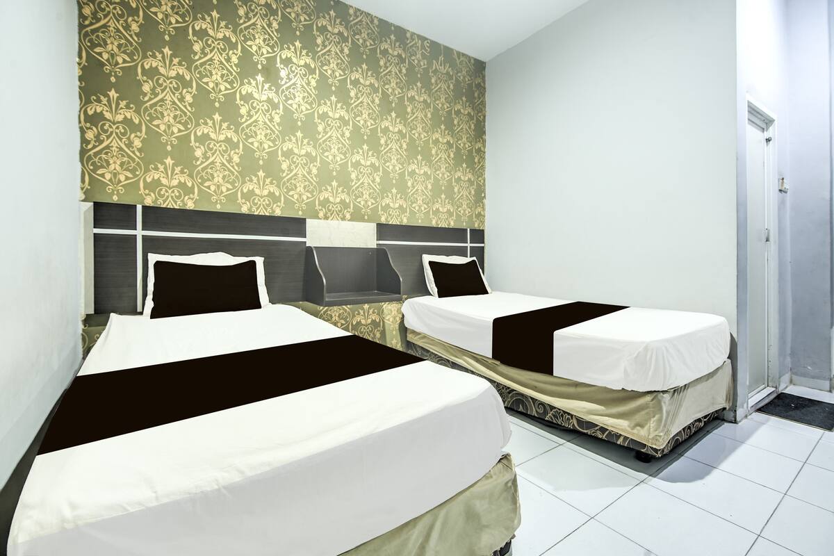 A hotel room with two beds, a patterned wallpaper, and a door to the right.
