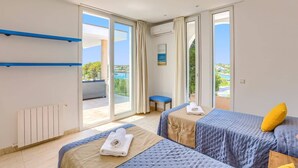 A hotel room with two beds, a view of the sea, and a balcony with a chair. - Villa Ses Arcades II by Villa Plus (Cala d'Or)