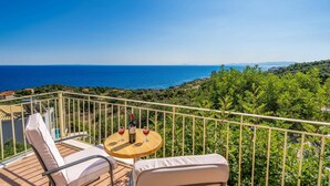A balcony with a table and chairs, overlooking a coastal view with the sea and greenery. - Villa Apollon by Villa Plus (Ionian Islands)