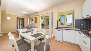 A modern kitchen with white cabinets, a black tiled backsplash, and a window with yellow frames. - Villa Apollon by Villa Plus (Ionian Islands)