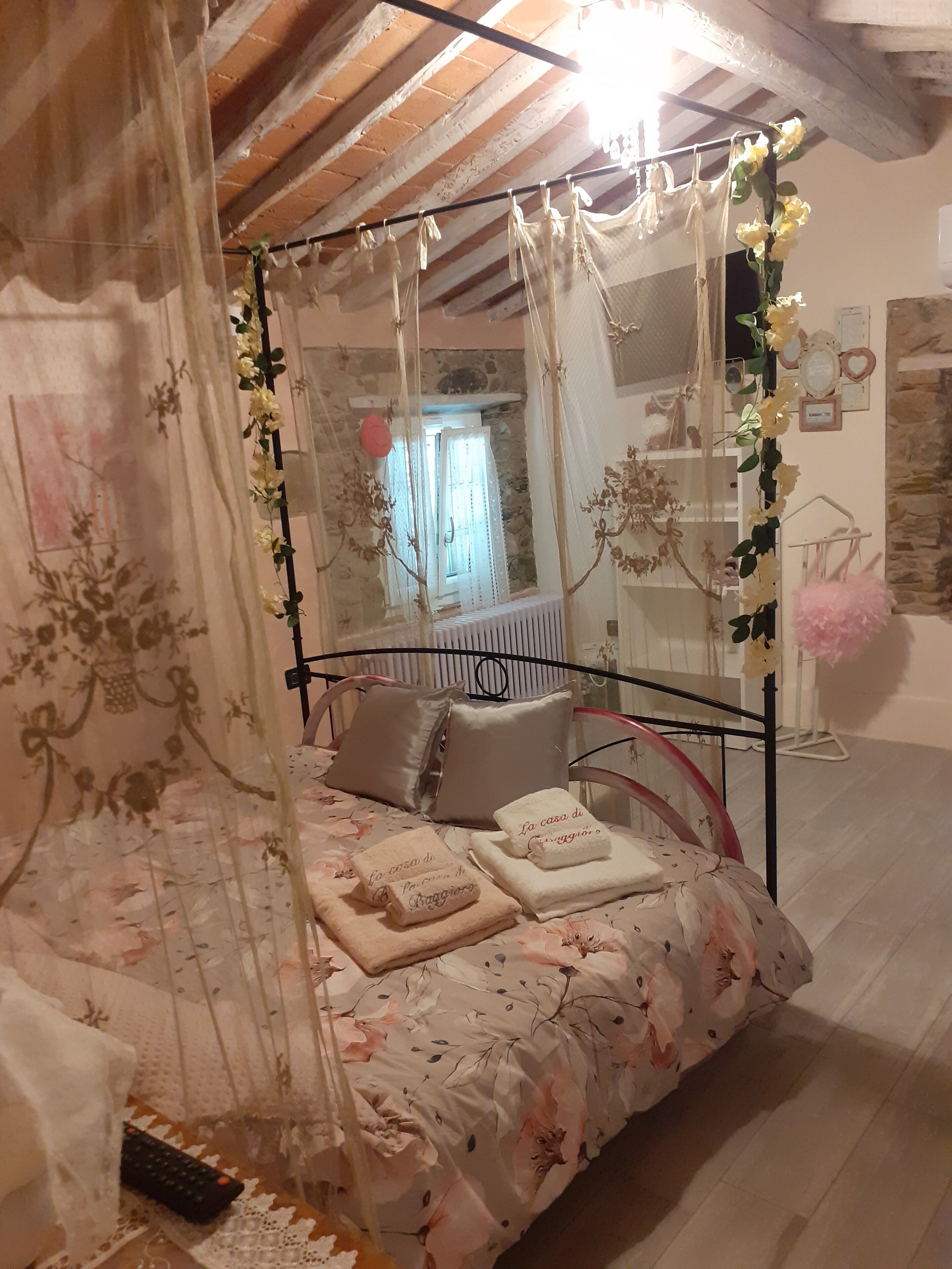 Una camera da letto con un letto a baldacchino, biancheria da letto floreale e vista su un muro di pietra e una finestra.