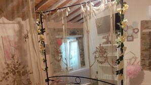 A bedroom with a canopy bed, floral bedding, and a view of a stone wall and window. - THE HOUSE OF BAGGIORO (Capannori)