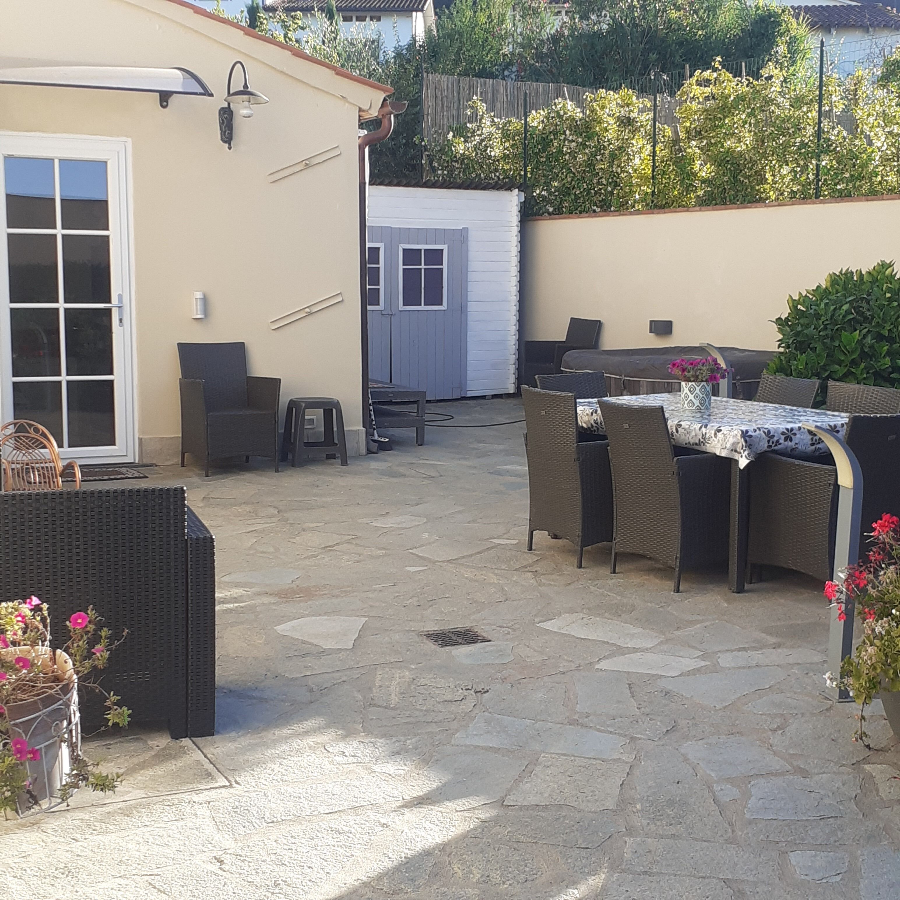 Una zona patio esterna con pavimento in pietra, mobili in vimini e un tavolo con tovaglia fantasia.